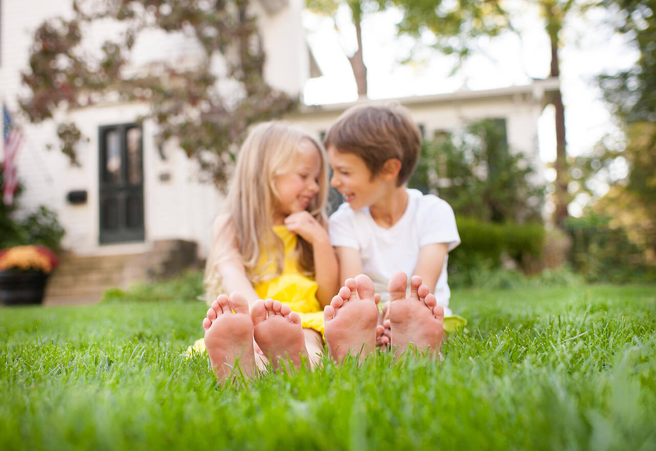 Children with bare feet sitting on lawn after organic lawn care treatment