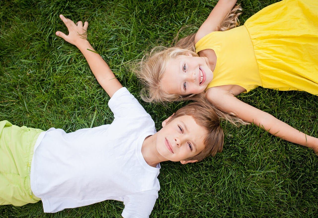 Two smiling children lying on lush organic green grass, enjoying a sunny day outdoors